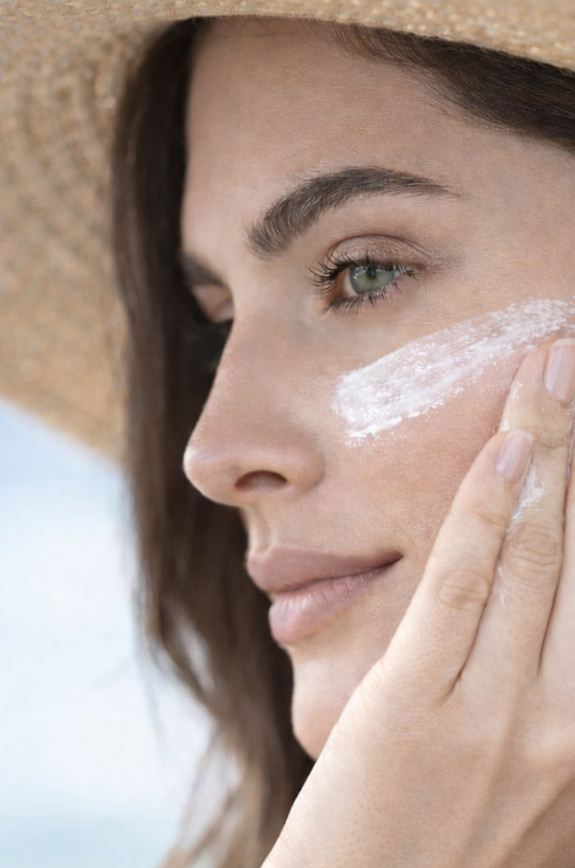 Woman applying sunscreen to her face with a blurred beach background